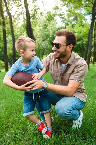 Счастливый отец и сын с американским футбольным мячом в парке — стоковое фото