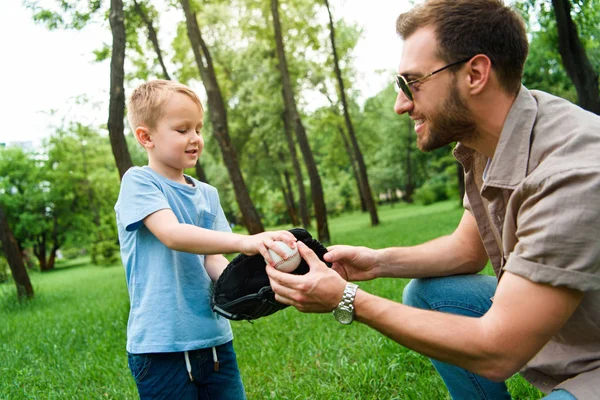 Padre dando hijo pelota de béisbol y guante en el parque - foto de stock