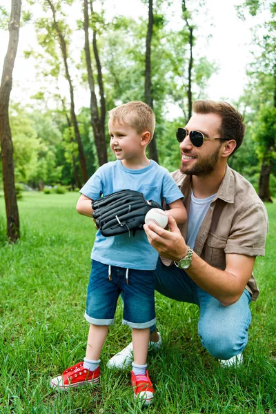 Отец обнимает сына бейсбольным мячом и перчаткой в парке — стоковое фото