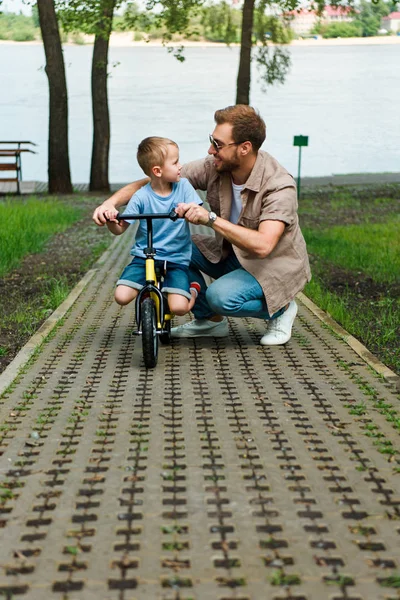 Отец и сын с маленьким велосипедом смотрят друг на друга в парке — стоковое фото