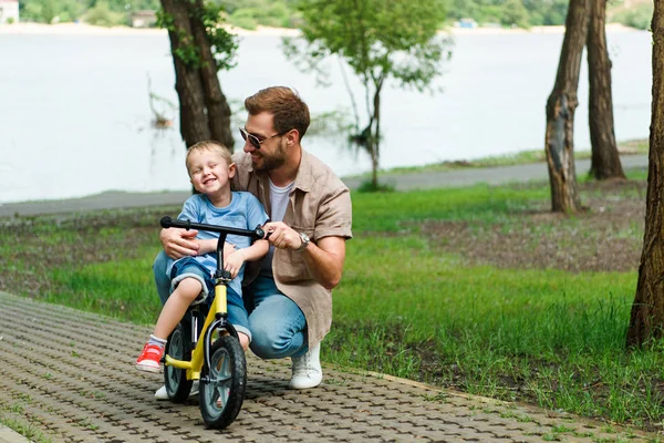 Padre felice insegnamento figlio in sella alla bicicletta al parco — Foto stock
