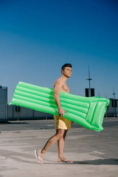 Handsome young shirtless man with inflatable bed on parking — Stock Photo