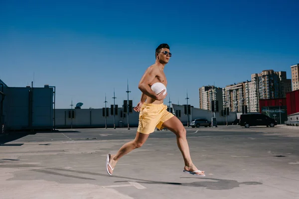 Молодий без сорочки чоловік біжить з волейбольним м'ячем на парковці — стокове фото