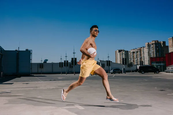 Joven hombre sin camisa corriendo con pelota de voleibol en el aparcamiento - foto de stock