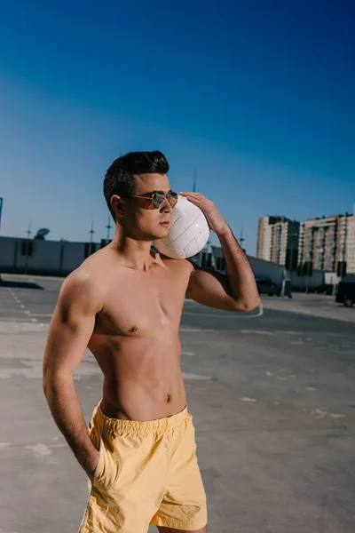 Joven hombre sin camisa sosteniendo pelota de voleibol en el estacionamiento - foto de stock