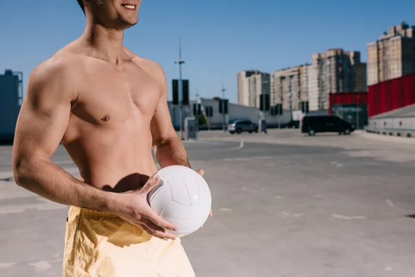 Plan recadré d'un jeune homme torse nu tenant une balle de volley-ball sur un parking — Photo de stock