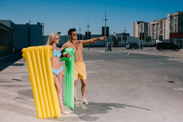 Happy young couple in beach clothes with inflatable beds on parking — Stock Photo