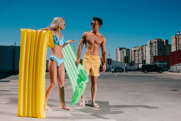 Atractiva pareja joven en ropa de playa con camas inflables en el aparcamiento - foto de stock