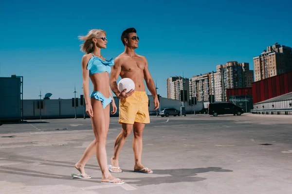 Jovem casal em roupas de praia com bola de vôlei no estacionamento — Fotografia de Stock