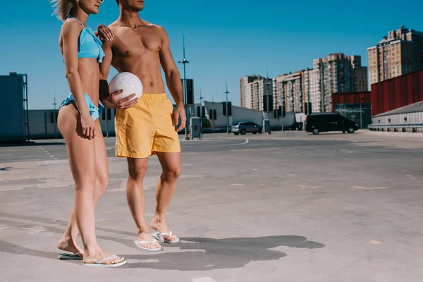 Cropped shot of young couple in beach clothes with volleyball ball on parking — Stock Photo