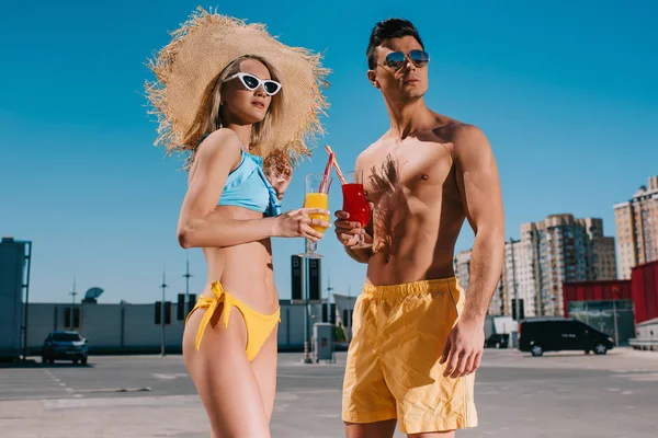 Beautiful young couple in beach clothes with refreshing cocktails standing on parking — Stock Photo