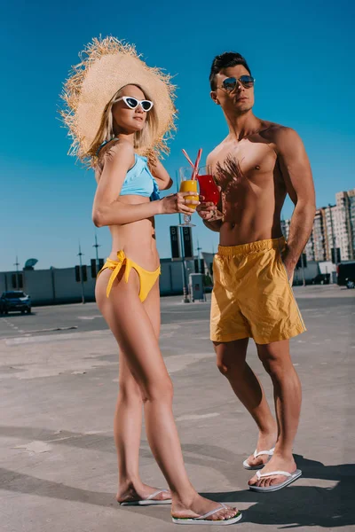 Attractive young couple in beach clothes with refreshing cocktails standing on parking — Stock Photo