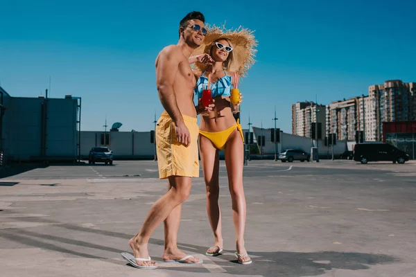 Jeune couple en vêtements de plage avec des cocktails rafraîchissants debout sur le parking — Photo de stock