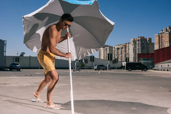 Attractive young man putting beach umbrella in asphalt on parking — Stock Photo