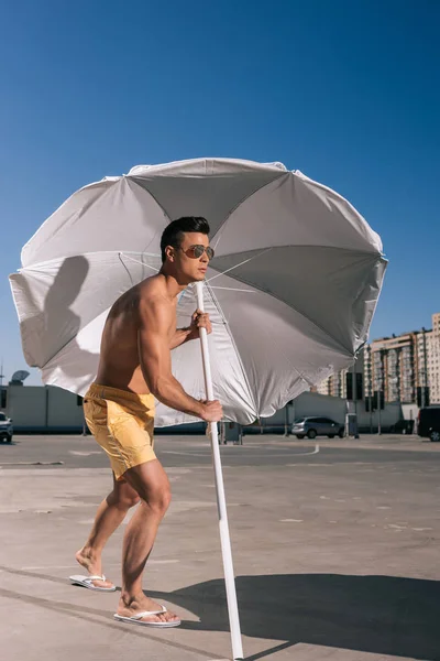 Bonito jovem colocando guarda-chuva praia em asfalto no estacionamento — Fotografia de Stock