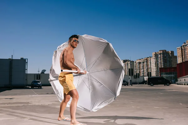 Привабливий молодий без сорочки чоловік з пляжною парасолькою на парковці — стокове фото