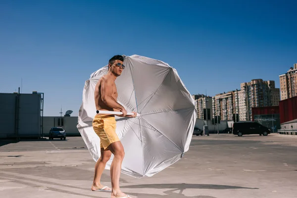 Attractive young shirtless man with beach umbrella on parking — Stock Photo