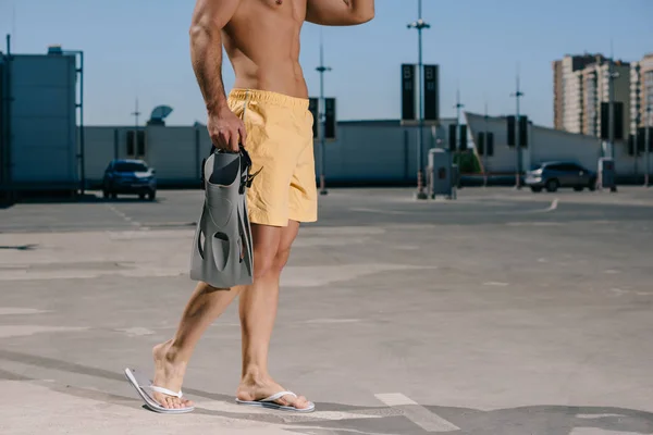 Cropped shot of shirtless man in swimming shorts with flippers on parking — Stock Photo