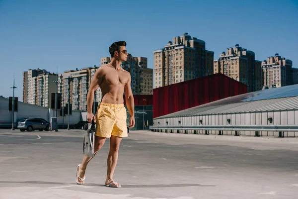 Handsome young shirtless man in swimming shorts with flippers on parking — Stock Photo