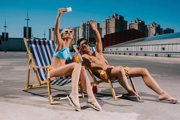 Young couple relaxing on sun loungers with cocktails and taking selfie on parking — Stock Photo