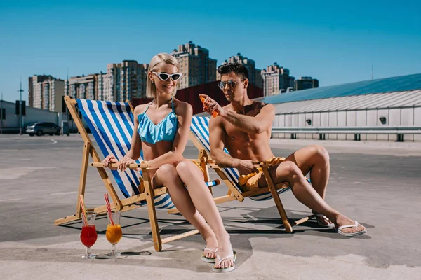 Young attractive man applying sunscreen lotion on girlfriends back on parking — Stock Photo