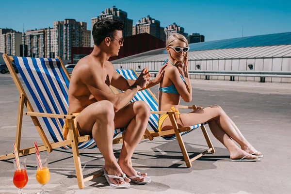 Young man applying sunscreen lotion on girlfriends back on parking — Stock Photo