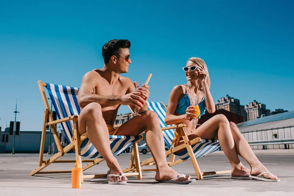 Young couple with refreshing cocktails sitting on sun loungers on parking — Stock Photo