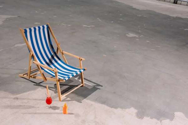 High angle view of sun lounger with cocktail and lotion on asphalt — Stock Photo