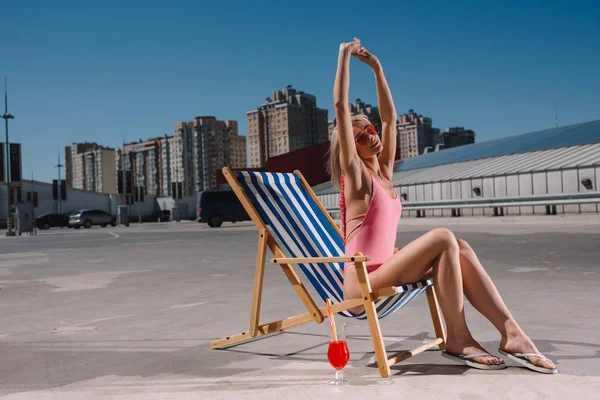 Beautiful young woman stretching while relaxing in sun lounger on parking — Stock Photo