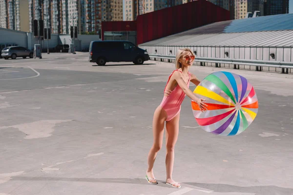 Bella giovane donna in costume da bagno con pallone da spiaggia colorato sul parcheggio — Foto stock