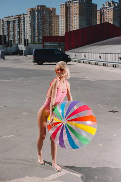 Attractive young woman in swimsuit with colorful beach ball on parking — Stock Photo