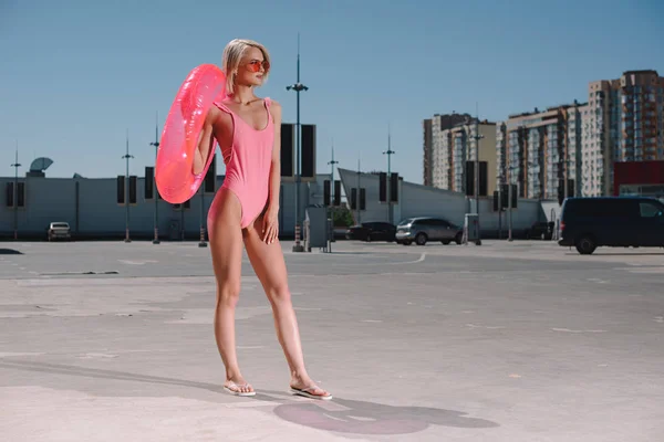 Stylische junge Frau im Badeanzug mit aufblasbarem Ring auf dem Parkplatz — Stockfoto