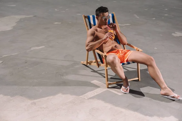 High angle view of young shirtless man drinking cocktail while relaxing in sun lounger on asphalt — Stock Photo