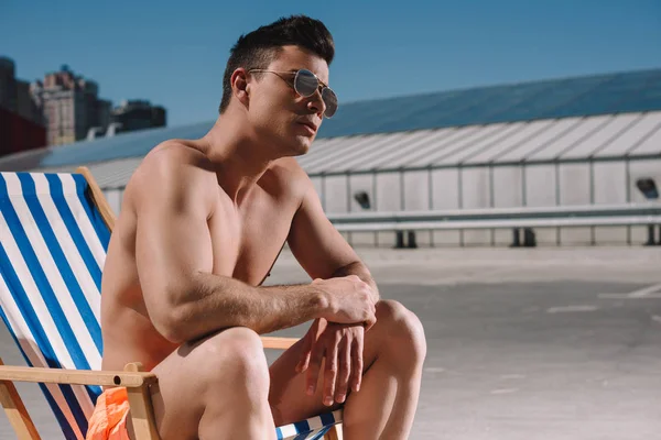 Handsome young shirtless man sitting on sun lounger on parking — Stock Photo