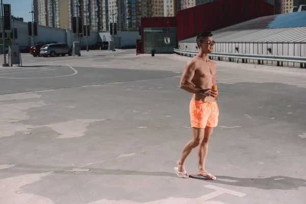 Schöner junger Mann ohne Hemd in Badehose mit Cocktail auf dem Parkplatz — Stockfoto