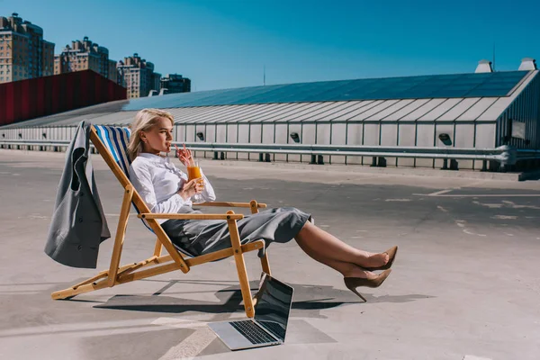 Belle jeune femme d'affaires en tenue formelle assis dans une chaise longue et cocktail à boire sur le parking — Photo de stock