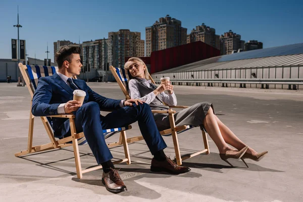 Jovens pessoas de negócios felizes relaxando em espreguiçadeiras com café para ir no estacionamento — Fotografia de Stock