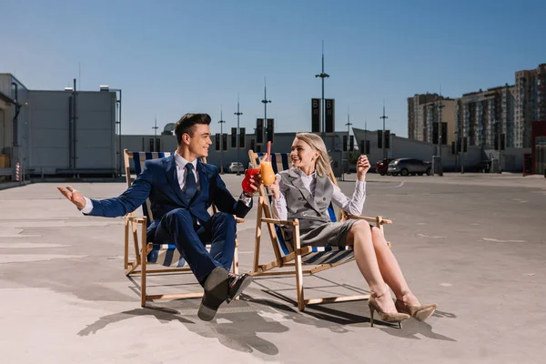 Junge Geschäftsleute entspannen sich auf Sonnenliegen, klirren Gläser mit Cocktails auf dem Parkplatz — Stockfoto