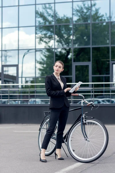 Young businesswoman with digital tablet in hands standing near retro bicycle on street — Stock Photo