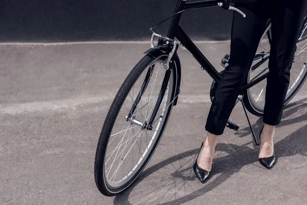 Tiro cortado de mulher de negócios em terno e saltos altos de pé perto de bicicleta retro na rua — Fotografia de Stock