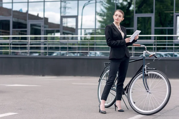 Young businesswoman with digital tablet standing near retro bicycle on street — Stock Photo