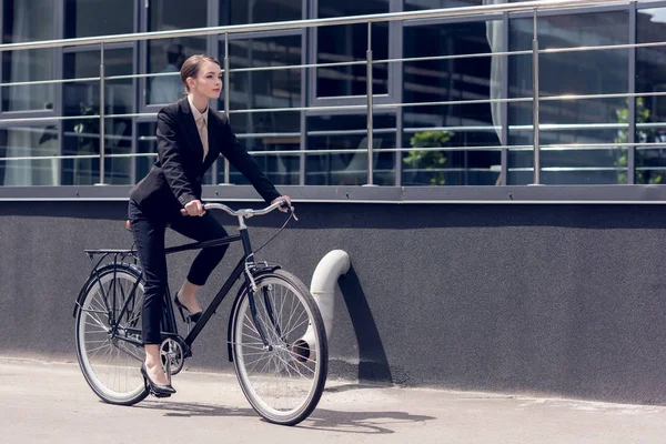 Side view of young stylish businesswoman in suit riding retro bicycle — Stock Photo