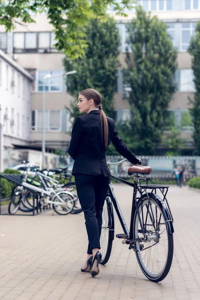 Vista trasera de la joven mujer de negocios de pie cerca de bicicleta retro en la calle - foto de stock