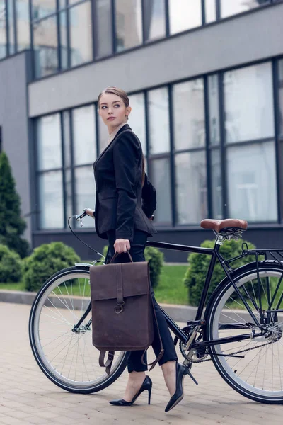 Vista lateral de la joven empresaria con maletín y bicicleta retro en la calle - foto de stock
