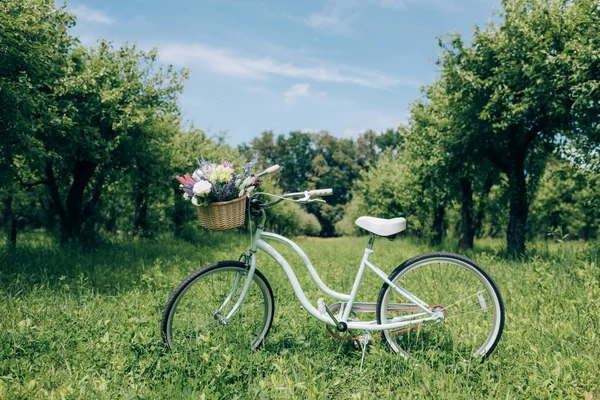 Foco seletivo de bicicleta retro com cesta de vime cheia de flores no campo — Fotografia de Stock