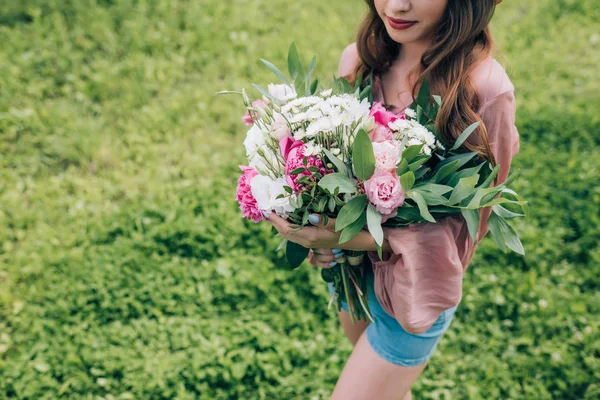 Partial view of young woman holding bouquet of flowers in hands in park — Stock Photo