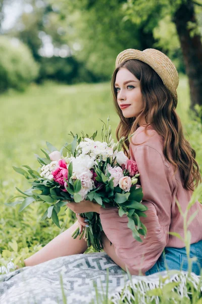 Vista laterale di bella donna pensosa con mazzo di fiori appoggiati su coperta in parco — Foto stock