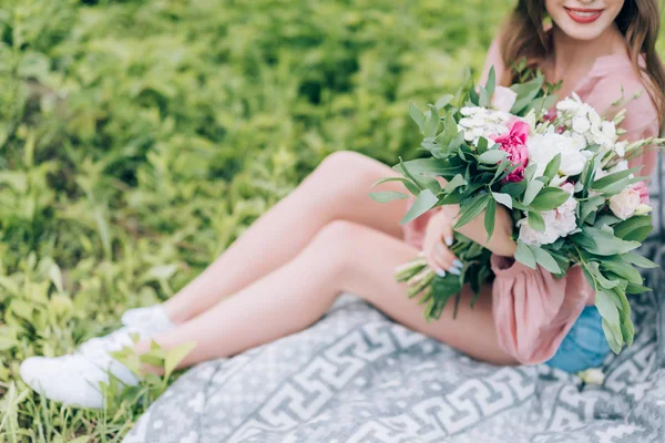 Colpo ritagliato di donna sorridente con mazzo di fiori appoggiati su coperta su erba verde nel parco — Foto stock