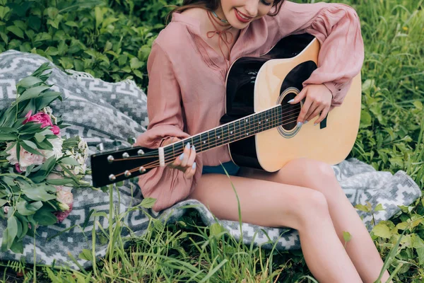 Recortado tiro fo mujer con guitarra acústica descansando sobre manta con ramo de flores en el parque - foto de stock