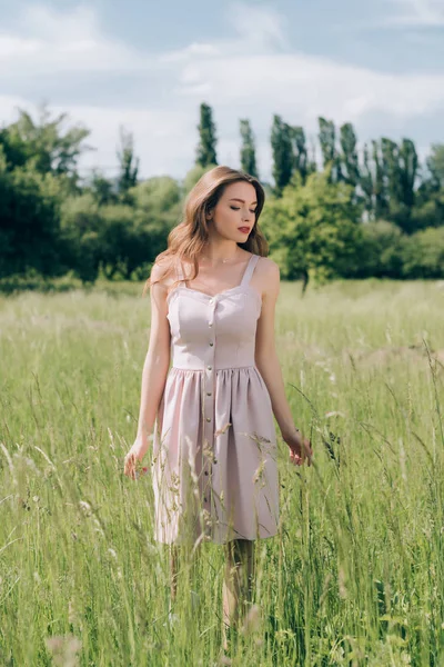Young pensive woman in stylish dress with long hair walking in meadow alone — Stock Photo